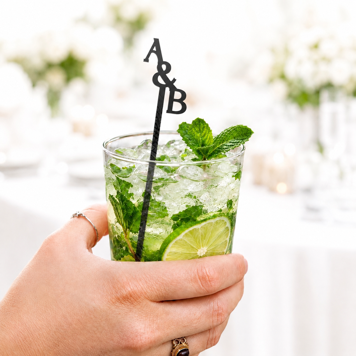 Black A&B stacked initials stir stick in a mojito held by hand