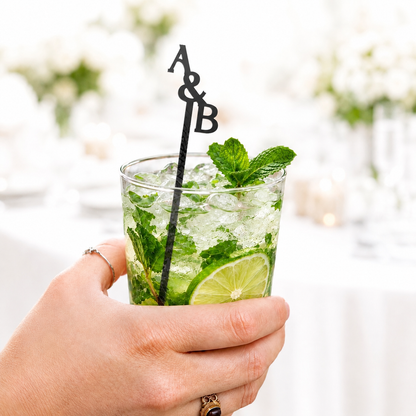 Black A&B stacked initials stir stick in a mojito held by hand