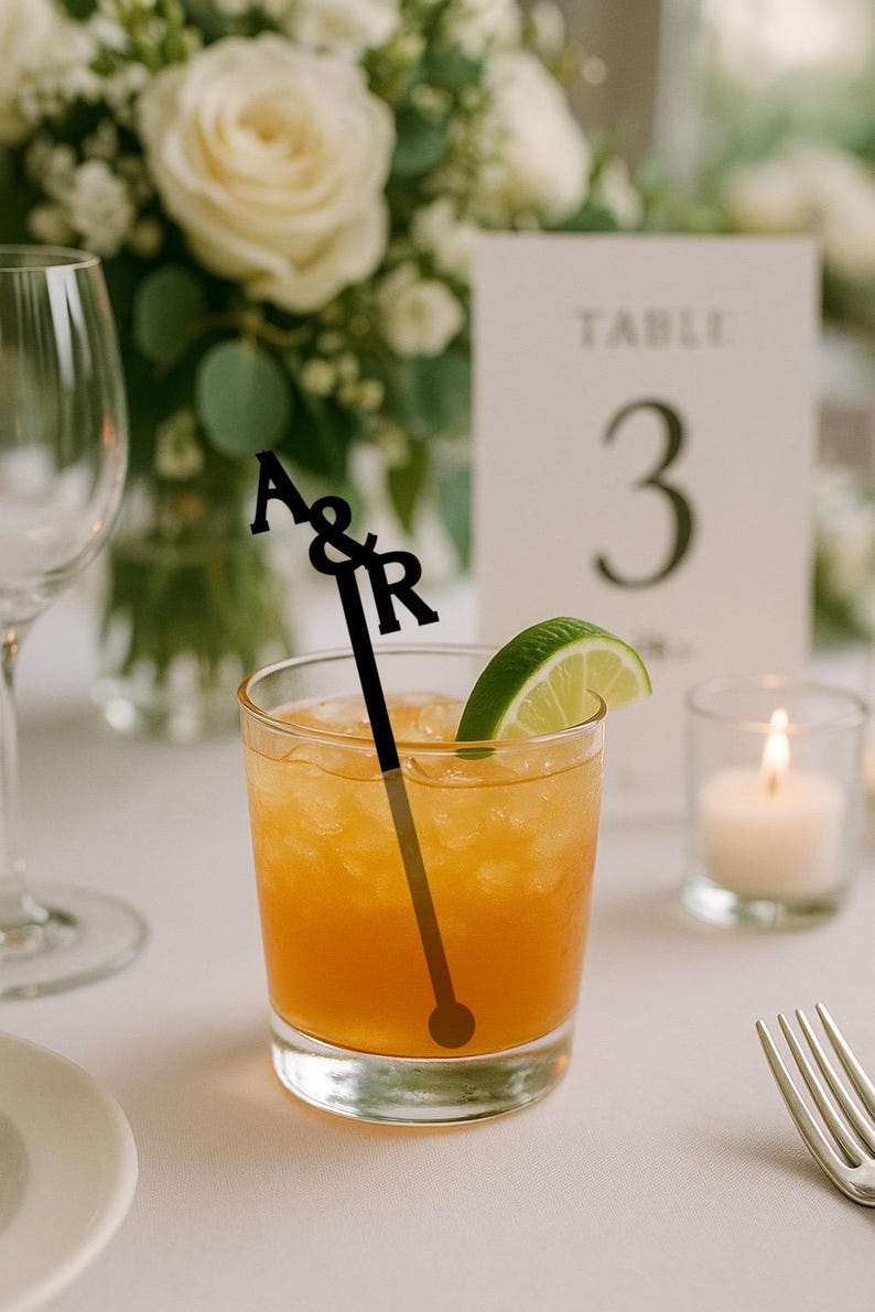Stacked initials A&R stir stick in a cocktail beside a wedding table number